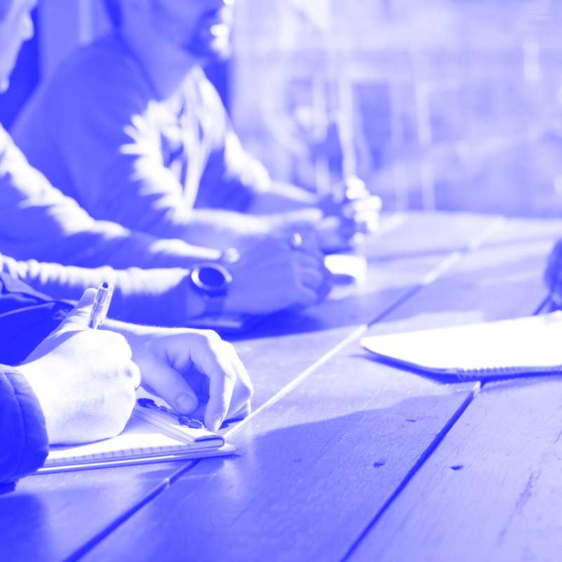 Menschen sitzen an einem Tisch mit Schreibutensilien vor sich, Nahaufnahme hände