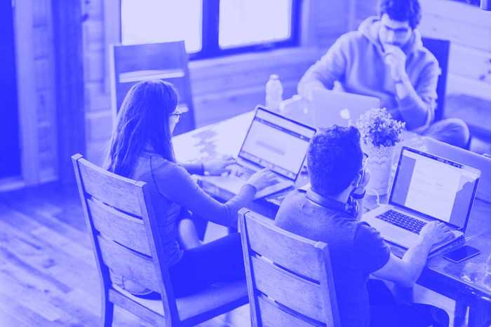 Menschen sitzen an einem Tisch und arbeiten an Computern